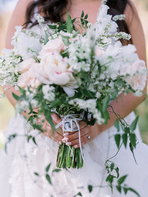 Bride holding blush and ivory floral bouquet with portraits attached to the handle of the bouquet.